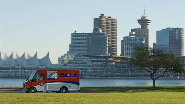 A Canada Post truck with the Vancouver city skyline in the background.