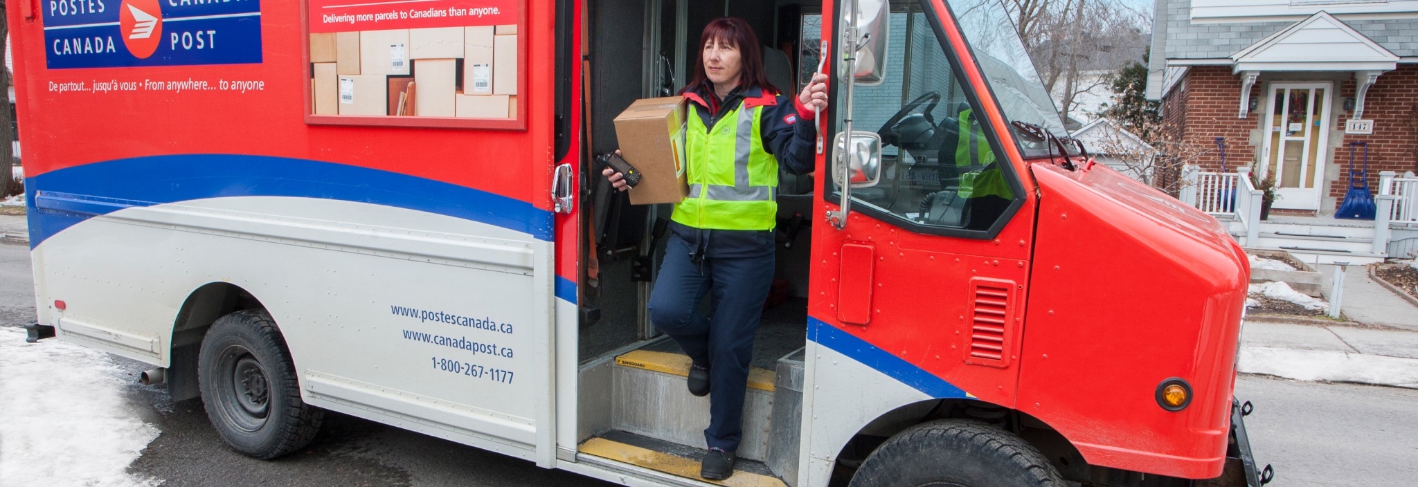 Delivery agent stepping out of a Canada Post truck in a residential neighbourhood to deliver a package