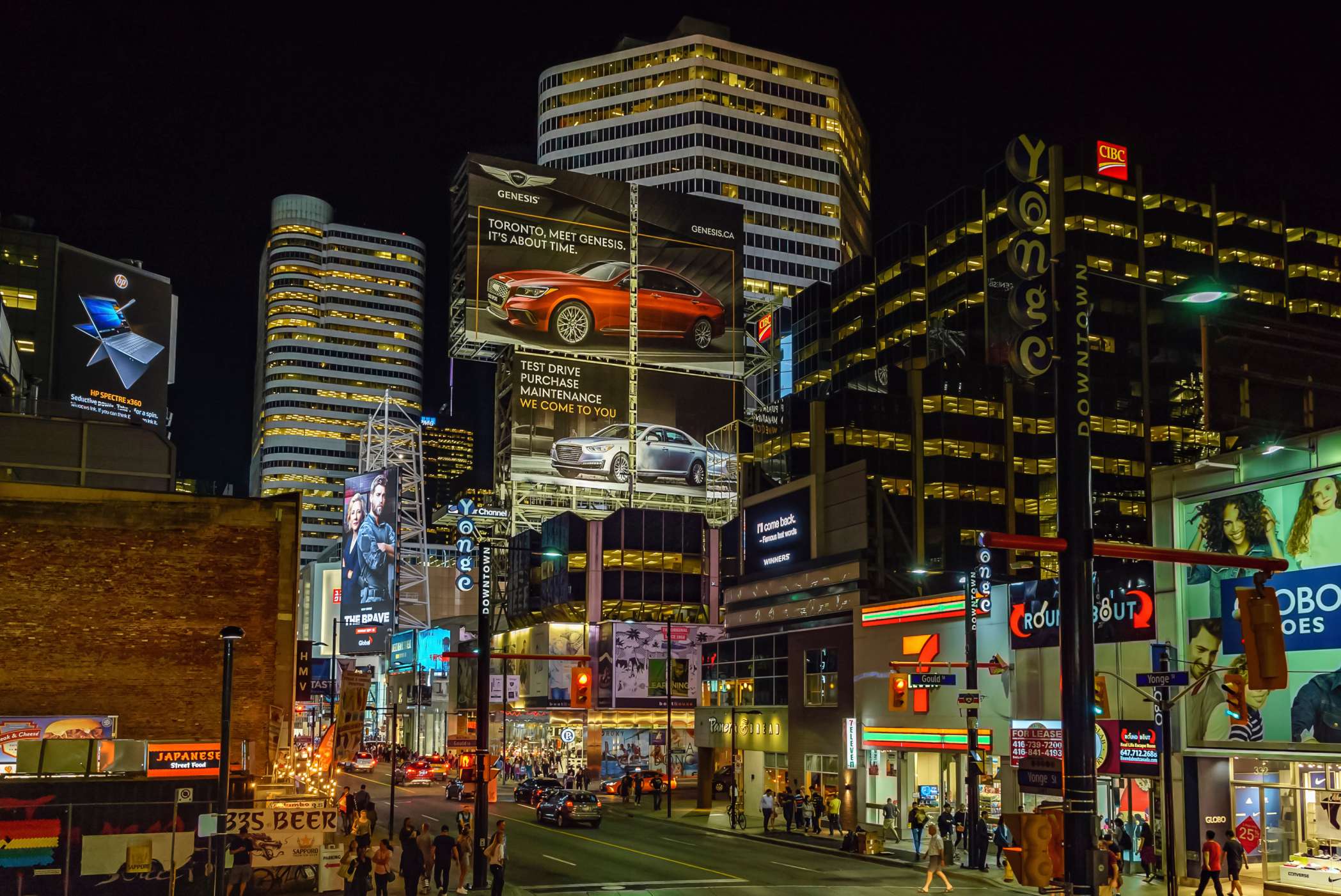 Street view of downtown Toronto after dark, with bright, illuminated billboards and signs.