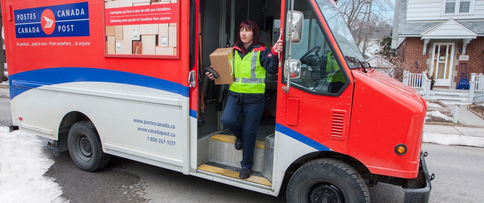 Agente de livraison sortant d’un camion de Postes Canada dans un quartier résidentiel pour livrer un colis