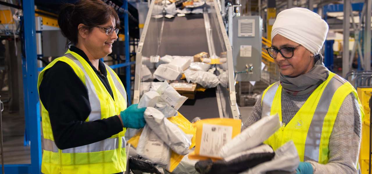 Deux employées de Postes Canada portant un gilet de sécurité jaune vif trient des colis et des enveloppes