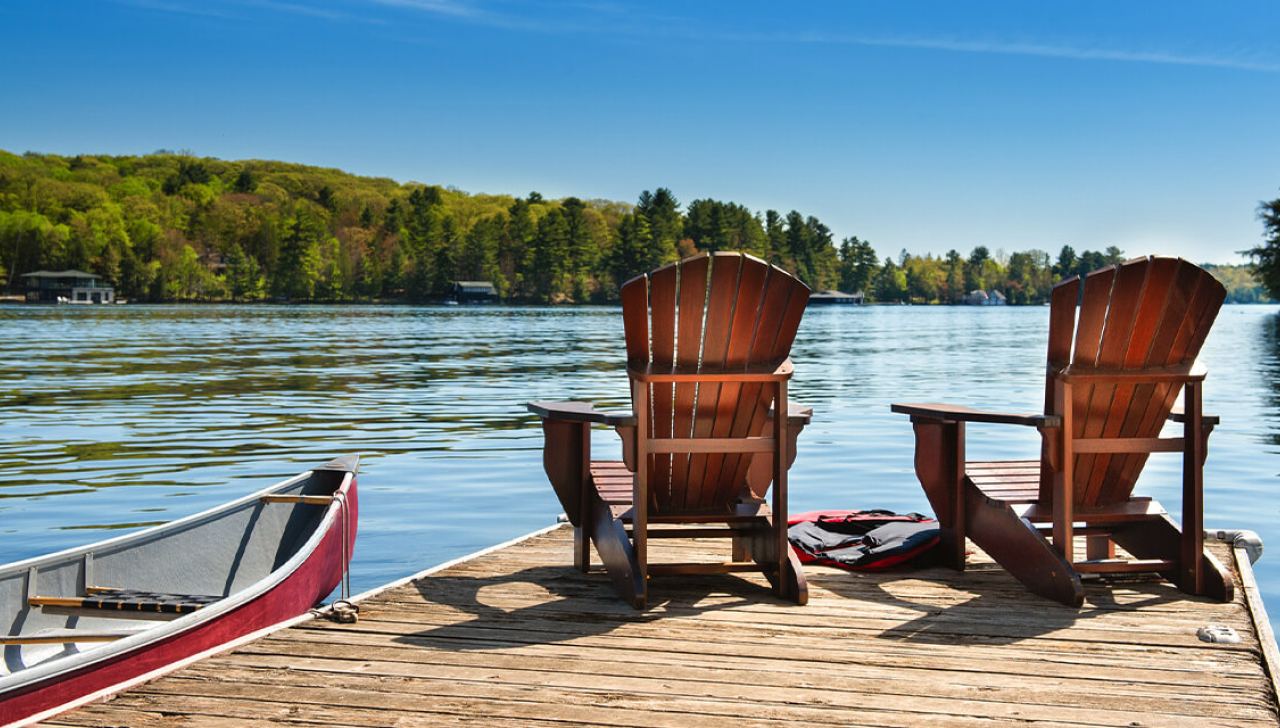 Deux chaises en bois reposent sur un quai au bord d’un lac, à côté d’un canot.