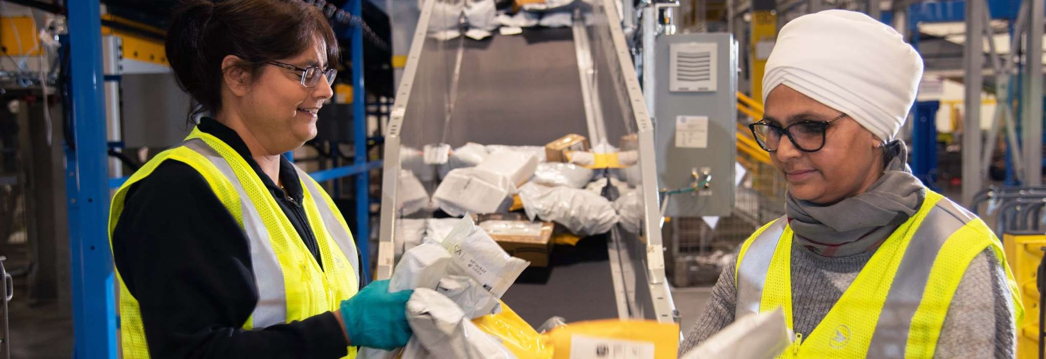 Deux employées de Postes Canada portant un gilet de sécurité jaune vif trient des colis et des enveloppes 