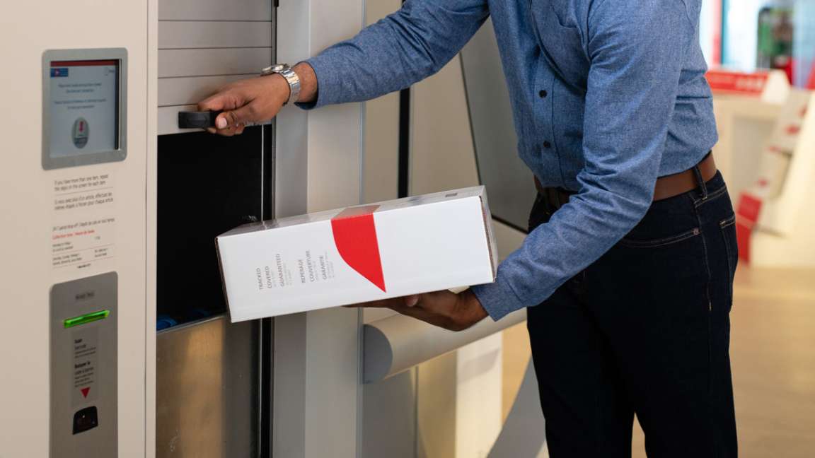 Un homme utilise une boîte de dépôt de colis automatisée à un bureau de poste pour poster une boîte à tarif fixe